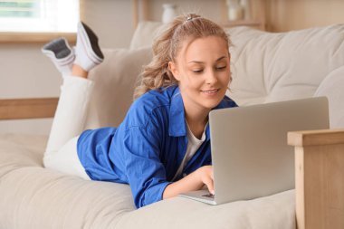 Evdeki kanepede dizüstü bilgisayar kullanan güzel sarışın kadın.