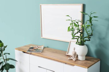 Oturma odasındaki nane duvarının yanındaki çekmecelerde yeşil dallı vazo ve fotoğraf çerçeveli.