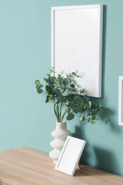 Oturma odasındaki nane duvarının yanındaki çekmecelerde yeşil dallı vazo ve fotoğraf çerçeveli.