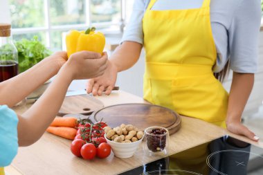 Genç anne mutfakta oğlundan dolma biber alıyor, yakın plan.