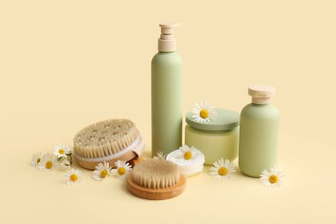 Papatya çiçekleri, masaj vücut fırçaları, kavanoz ve bej arka planda kozmetik ürünler içeren kompozisyon, yakın plan