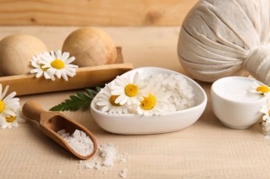 Bir kase deniz tuzu, papatya çiçeği ve ahşap arka planda masaj topları içeren kompozisyon, yakın plan.