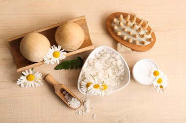 Bir kase deniz tuzu, papatya çiçeği ve ahşap arka planda masaj topları içeren kompozisyon, yakın plan.