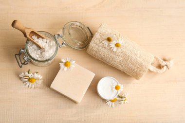 Sabun barı, papatya çiçekleri ve ahşap arka planda kozmetik ürünleri kavanozları, yakın plan.