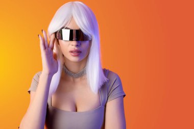 Turuncu arka planda VR gözlüklü peruklu genç kadın, yakın plan.