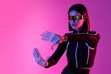 Pembe arka planda VR gözlüğü kullanan genç bir kadın.