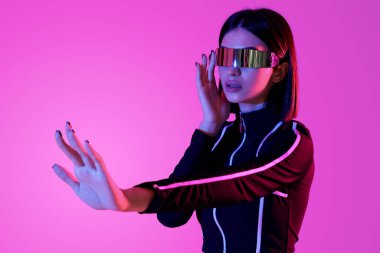 VR gözlüklü genç kadın pembe arka planda sanal ekran kullanıyor