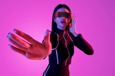 VR gözlüklü genç kadın pembe arka planda sanal ekran kullanıyor