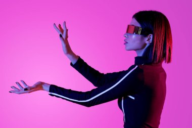 VR gözlüklü genç kadın pembe arka planda sanal ekran kullanıyor