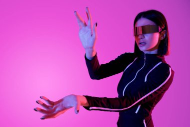 VR gözlüklü genç kadın pembe arka planda sanal ekran kullanıyor