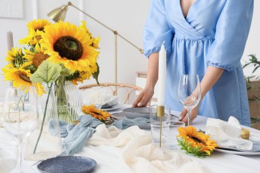 Yemek masasını güzel ayçiçekleriyle süsleyen genç bir kadın.