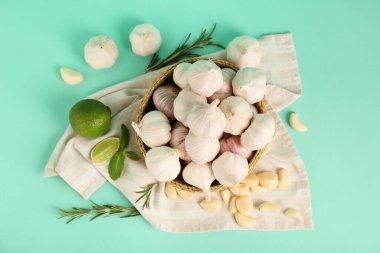 Taze sarımsaklı hasır kase, biberiye ve turkuaz arka planda limon.