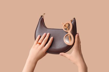 El çantalı ve bej arka planda güneş gözlüklü bir kadın eli.