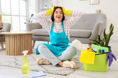 Temizlik malzemeleriyle stresli kadın hademe odada oturuyor.
