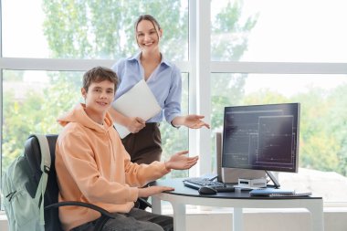 Erkek öğrenci okulda bilgisayar laboratuarında öğretmenle çalışıyor.