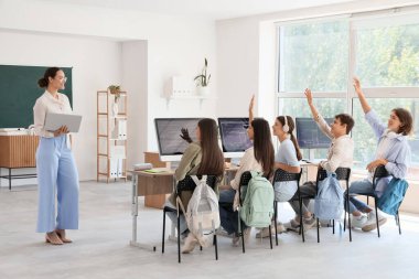 Okulun bilgisayar laboratuvarında öğrencilere ders veren bayan öğretmen.