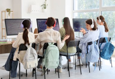Kulaklık takmış bir grup genç öğrenci okul bilgisayar laboratuvarında çalışıyor.