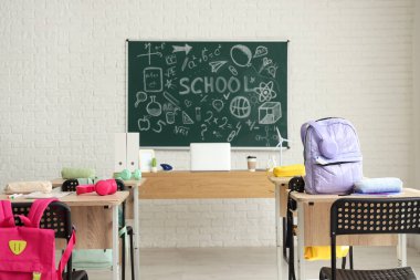 Sıraları, sırt çantaları ve tahtası olan sınıfın içi.