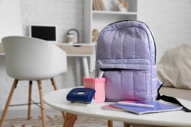 Oturma odasındaki masanın üzerinde kırtasiye malzemesi olan leylak rengi sırt çantası.
