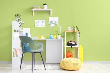 Odadaki yeşil duvarın yanında rafları ve çizimleri olan çocuk işyeri.