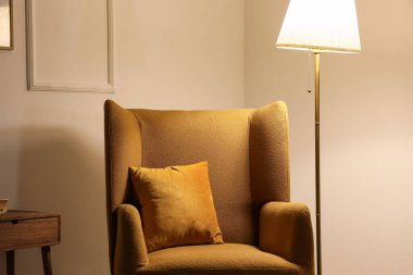 Karanlık odada rahat koltuk ve parlayan lamba.