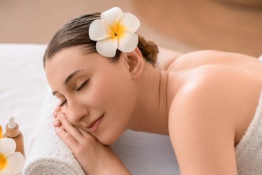 Güzel, genç, mutlu bir kadın, beyaz bir çiçekle kaplıcadaki kanepede yatıyor.