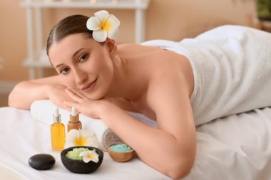 Beyaz tesisat çiçekleri, deniz tuzu ve kozmetik yağıyla kaplıca salonundaki kanepede uzanan güzel, genç ve mutlu bir kadın.