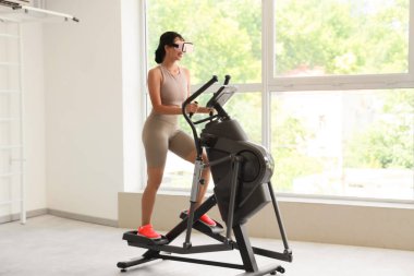 Spor salonunda spor bisikletli, VR gözlüklü Afro-Amerikalı bir kadın.