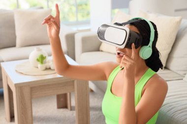 Evde VR gözlük kullanan Afro-Amerikalı bir kadın.