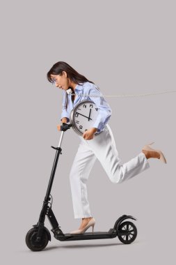 Gri arka planda elektrikli scooter kullanan Asyalı genç bir iş kadını.