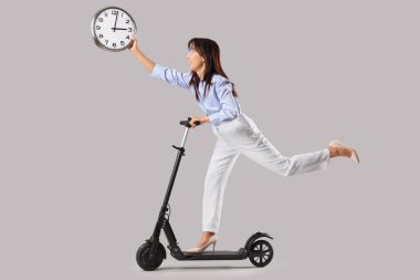 Gri arka planda elektrikli scooter kullanan Asyalı genç bir iş kadını.