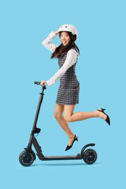 Mavi arka planda elektrikli scooterlı genç Asyalı iş kadını