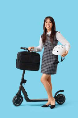 Mavi arka planda çantalı ve elektrikli scooter kullanan Asyalı genç bir iş kadını.