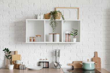 Mutfaktaki beyaz tuğla duvarda mutfak gereçleri olan tezgah ve raf.