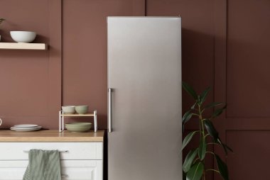 Mutfakta kahverengi duvarın yanındaki modern buzdolabı.