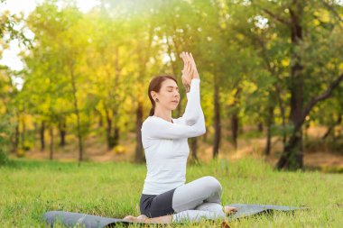 Genç kadın parkta yoga yapıyor.