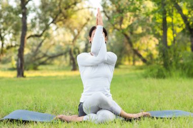 Genç kadın parkta yoga yapıyor.