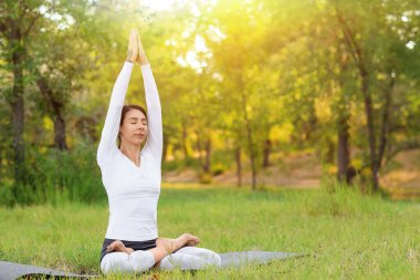 Genç kadın parkta yoga yapıyor.