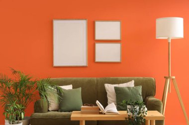 Şık oturma odasının içinde lamba, yeşil kanepe ve boş çerçeveler var.