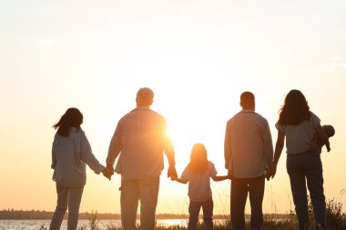 Gün batımında, nehrin kenarında el ele tutuşan büyük aile silueti.