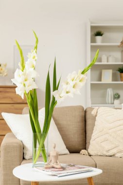 Oturma odasında üzerinde gladiolus çiçekleri, heykelcikler ve dergiler olan bir vazo.