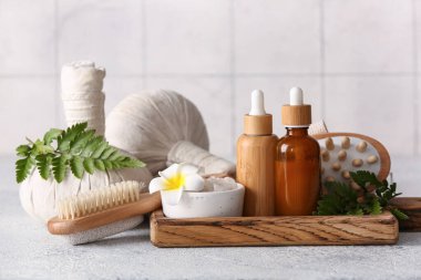 Tepsisi, bitkisel poşetleri, gri grunge masasında kozmetik ürünleri olan spa kompozisyonu, karo duvarın yanında, yakın plan.