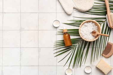 Tropikal yapraklı spa kompozisyonu, yanan mumlar ve beyaz fayans zemininde bir şişe kozmetik ürünü.