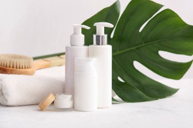 Beyaz arka planda tropikal yaprak, şişe ve kozmetik ürünler içeren spa kompozisyonu, yakın plan