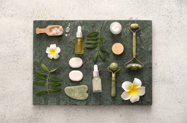 Tepsisi, yüz masajı aletleri, kavanoz ve bej grunge arka planda bir şişe kozmetik ürünü içeren spa kompozisyonu