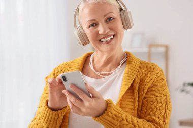 Evde radyo dinleyen kulaklıklı yaşlı bir kadın.