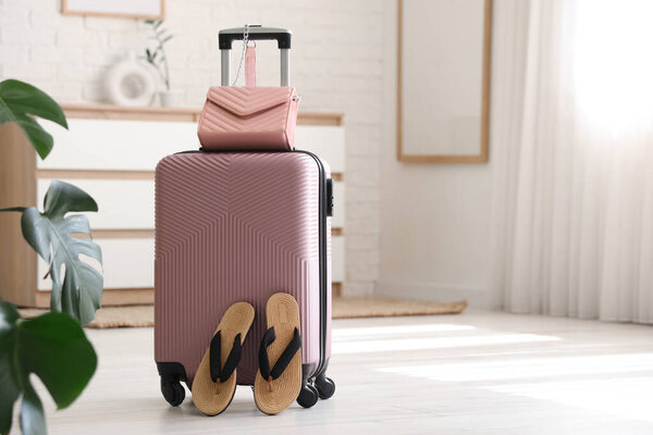 Чемодан и стильные флип-флопы на полу в гостиничном номере