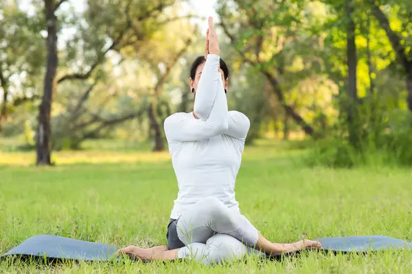Genç kadın parkta yoga yapıyor.