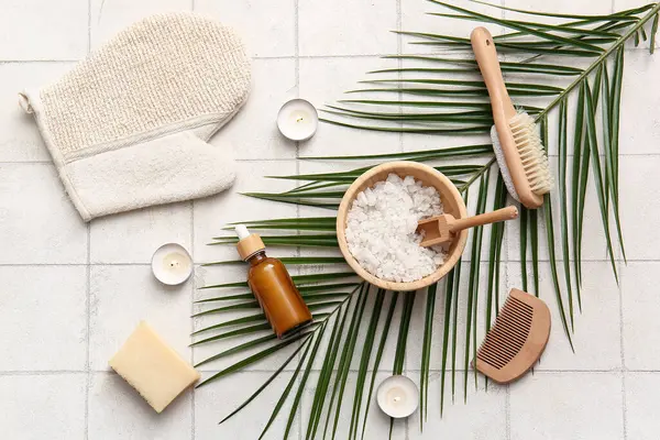 Tropikal yapraklı spa kompozisyonu, yanan mumlar ve beyaz fayans zemininde bir şişe kozmetik ürünü.