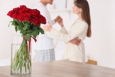 Masada kırmızı güller olan vazo, yatak odasında dans eden çifte karşı, yakın plan.